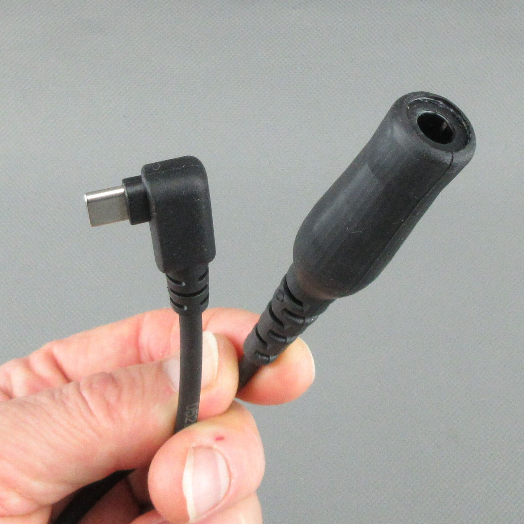 Main tenant le câble adaptateur StarCom1 FLX2, avec mise au point sur la fiche USB-C coudée et la prise femelle TP-120 (compatible Nexus® / Amphenol®) pour le raccordement de casques tactiques au câblage NATO.