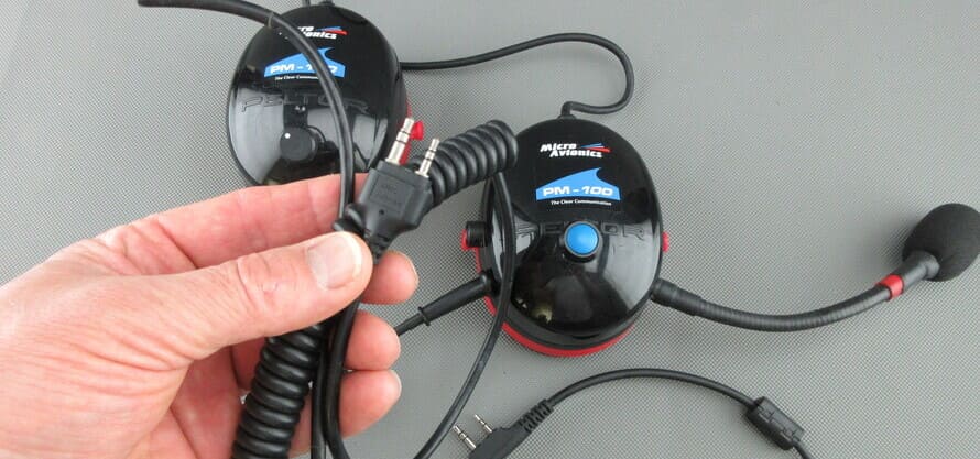 Un casque MicroAvionics® avec câble de connexion radio, montrant le connecteur radio tenu dans une main.
